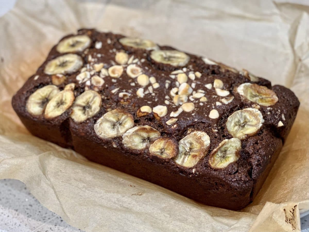 A loaf of cocoa banana bread with banana slices and hazelnuts on top